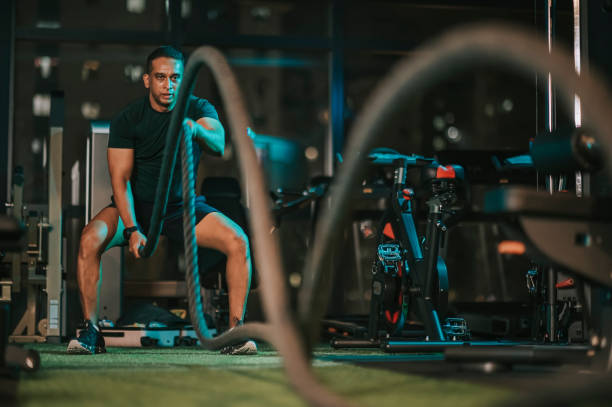 Asian Indian Mid Adult macho man practicing battle rope in gym